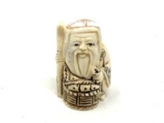 A Japanese carved bone netsuke - Village elder with a basket at his feet.
