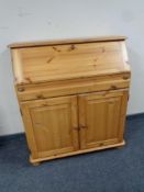 A pine writing bureau fitted double door cupboard beneath