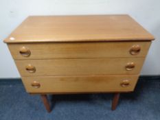 A mid 20th century teak three drawer chest on raised legs