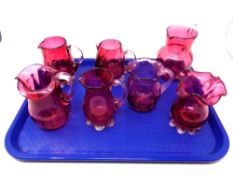 A tray containing seven antique cranberry glass jugs