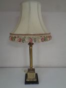 An antique brass Corinthian column table lamp on a black marble base