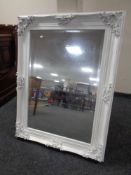 An ornate white painted bevelled overmantel mirror