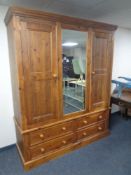 A contemporary pine double door wardrobe fitted with a central mirrored panel door and four drawers