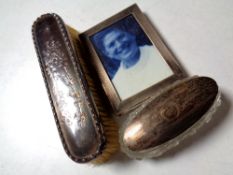 A silver photo frame, silver-backed brush, silver-topped cut glass dressing table jar.