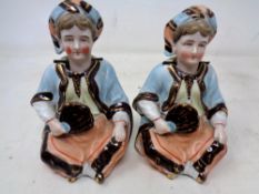 A pair of bisque nodding head figures modelled as seated gentlemen holding fans
