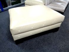 An oversized footstool upholstered in cream leather.