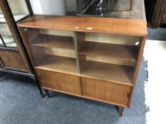 A 20th century teak sliding glass door bookcase fitted with cupboards below on raised legs.