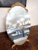 An oval frameless dressing table mirror on gilt wood stand.