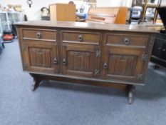 A triple door oak linen fold sideboard on raised legs fitted with drawers above.