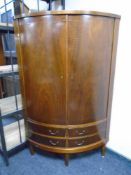 A walnut double door bowfront corner cabinet fitted with doors beneath