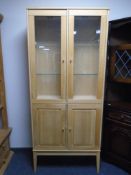 An Ikea double door display cabinet on raised legs in oak finish