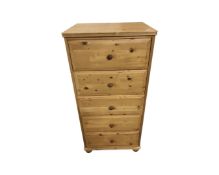 A contemporary narrow pine five drawer chest on bun feet,