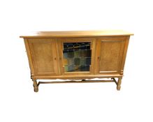 A blond oak triple door sideboard with stained glass panel door,