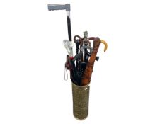 A cylindrical brass stick pot containing walking sticks, tourist boomerang, umbrella etc.