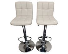 A pair of contemporary chrome gas lift barstools upholstered in cream vinyl.