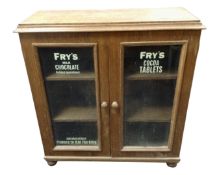 An oak double door cabinet on bun feet bearing Fry's Milk Chocolate advertising.