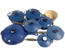 A crate containing eight blue cast iron Le Creuset pans and oven dishes, seven with lids.