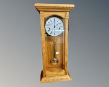 A contemporary pine wall clock with pendulum and key by Hermle.