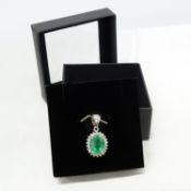 An 18ct white gold oval emerald and diamond cluster pendant, boxed