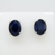 A pair of treated oval-cut sapphire solitaire ear studs in silver, with butterfly backs