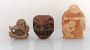 A Meiji period wooden netsuke of a boy playing a flute, 3.5 cm h and a noh mask netsuke, 4 x 4 cm,