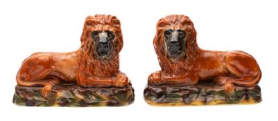 A pair of large Staffordshire brown glazed pottery recumbent lions with glass eyes and on rocky
