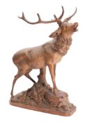 A Black Forest carved linden wood model of a stag with head raised, mounted on a rocky outcrop,