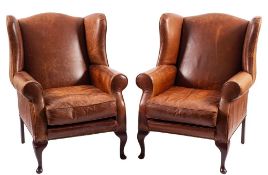 A pair of leather upholstered wing armchairs in George II style,