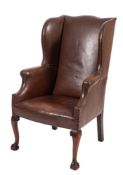 A studded leather wing armchair in George II taste, early 20th century; with outscrolled arms,