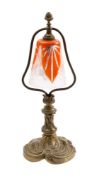 A brass table/student's lamp with foliate and scroll decorated base, orange and clear glass shade,