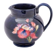 A Moorcroft pottery jug, tube lined in the Orchid pattern in red, yellow and green on a blue ground,