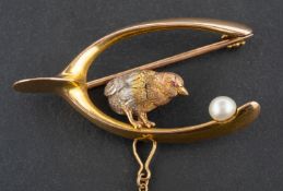 A brooch designed as a tri-colour chick within a wishbone beside a cultured pearl egg,