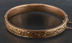 An early 20th century 9ct gold, hinged bangle, with engraved foliate and floral decoration,