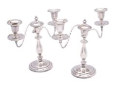 A pair of silver plated twin branch candelabra with scrolling branches terminating in urn-shaped