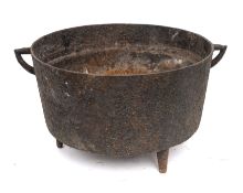 An iron circular open cooking pot with twin angular handles and tripod feet, 28cm diameter,