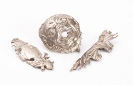 Three pieces of white metal pistol furniture: comprising a grotesque mask butt cap,