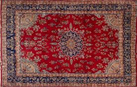 A Kirman Carpet, the red field with a central arabesque oval indigo and pastel blue medallion,