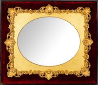 A gilt composition framed wall mirror in Rococo revival taste, the oval plate with sanded spandrels,