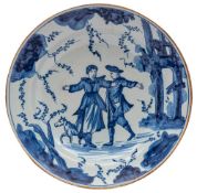 A Continental blue and white tin-glazed dish painted with two figures and a dog by ruins,