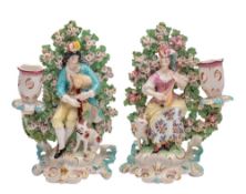 A pair of Derby shepherd and shepherdess candlestick groups with flowering bocage backgrounds,