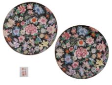 A pair of Chinese famille noire millefleurs plates painted with brightly coloured blooms on a black