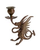 A brass griffin candlestick with foliate drip pan and red glass eyes, early 20th century, 17cm.