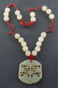 A carved, openwork nephrite pendant, depicting floral motifs on a green hardstone bead necklace,