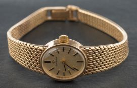 An Omega wristwatch, the oval, gilt dial with baton markers and hands, on integrated mesh bracelet,