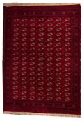A machine made carpet of Turkoman design, the red field with seven rows of quartered guls,