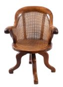 A Victorian walnut, birch and oak revolving office desk armchair with curved cane panel back,