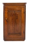 A George III oak hanging corner cupboard, circa 1800; with moulded cornice above a panel door,