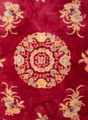 A Chinese carpet, 20th century; machine woven, with a central floral medallion on a cerise ground,