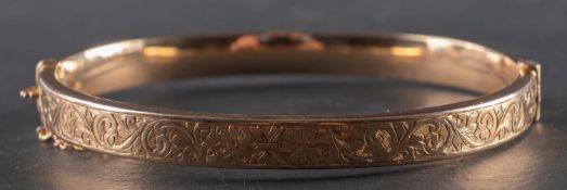 A 1940's, 9ct gold hinged bangle, decorated with foliate engraving, inner diameter ca.