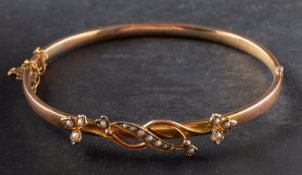 A hinged bangle, with floral spray motif as frontispiece, set with seed pearls, stamped '9CT',